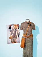 Glossy brown sweater, skirt and leather bag on clothes stand with photo of model