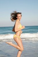 Ecstatic blonde woman wearing yellow bikini having fun while running on beach, smiling