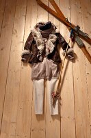 Brown fur jacket, long sweater, pants, ski and pole scattered on wooden floor