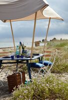 Outdoor-Möbel: Gartentisch mit aufge stecktem Sonnendach am Strand