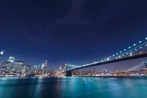 View of Brooklyn Bridge on East River at night in Manhattan, New York, USA