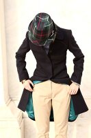 Woman wearing loden coat, pants and plaid hat standing, looking down