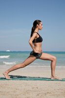 Woman wearing black bikini exercising on the beach, side view