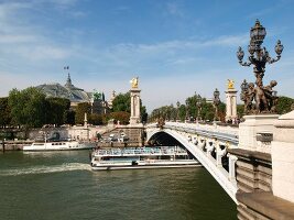 Ferry passing below of Pont Alexandre III over Seine river in Paris, France