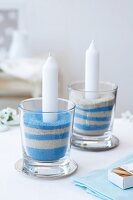 Lit candles in glasses with blue and white sand
