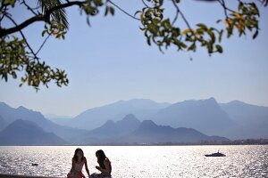 People sitting at promenade near sea and mountain range in Antalya, Turkey