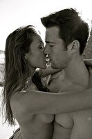 Seductive couple embracing each other and leaning against rock, black and white