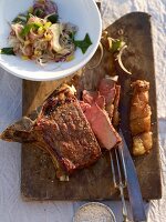 Grilled Argentinean steak sliced on wooden platter with onion salad in bowl