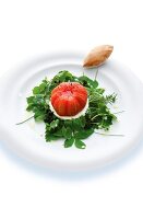 Skinned heirloom tomato on goat cheese and wild herbs salad on plate
