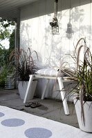 Bank of driftwood planks with white house wall, carpet and cushions on stool