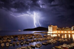 Boats moored on Dubrovnik old harbour with thunderstorm at night in Croatia