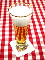Tall glass of beer with foam on beer mat kept on red and white checked napkin