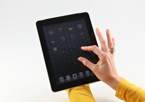 Frau in gelbem Oberteil hält Apple iPad und berührt das Display.