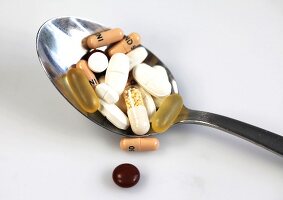 Close-up of spoon with various capsules and tablets on white background
