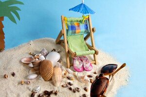 Urlaubsutensilien mit Liegestuhl, Muscheln und Palme im Sand