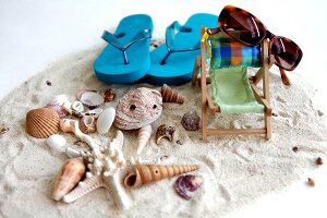 Urlaubsutensilien mit Liegestuhl und Muscheln im Sand