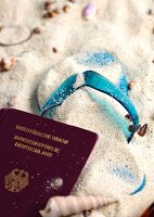 Close-up of flip flop and passport in the sand with sea shells