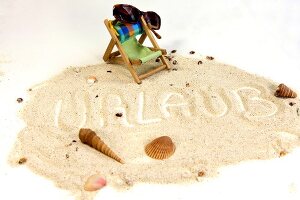 Holiday written in the sand with sea shells, deck chair and sunglasses around it