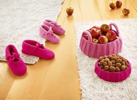 Filz-Hausschuhe und Häkelkörbe mit Äpfeln und Nüssen auf Teppich