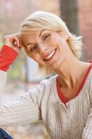 Pretty blonde woman with short hair wearing white sweater resting head on hand, smiling