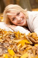 Blonde Frau in heller Jacke liegt auf Herbstlaub