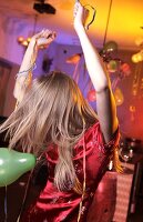 Happy woman wearing red satin dress celebrating while dancing at New Year's Eve party