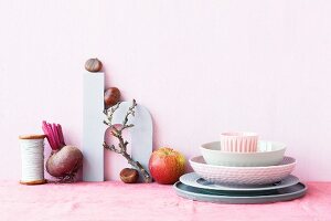 An arrangement featuring crockery, anpple, chestnuts, a beetroot and a decorative letter H