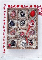 Red and black, hand-painted Easter eggs in a seedling tray lined with straw