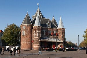 Tourists standing and cycling outside Waag monument in Nieuwmarkt, Amsterdam, Netherlands