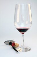 Glass of wine with cork and corkscrew on white background