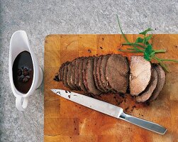 Slices of rhenish sauerbraten meat with knife on wooden board with knife