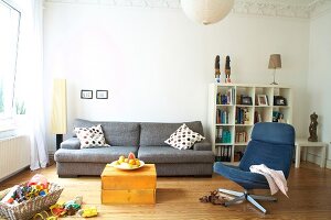 Gray couch, blue swivel chair and white shelves in living room with white walls
