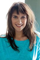 Portrait of pretty woman with brown hair and bangs wearing turquoise top, smiling