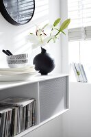White shelf with stacked plates and bowls, books and flower vase