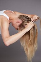 Side view of blonde woman braiding her hair in upside down position