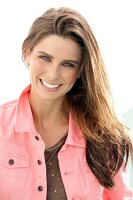 Portrait of pretty woman with dark hair wearing brown top and pink denim jacket, smiling