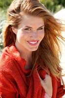 Portrait of attractive woman wearing pink top and red sweater sitting on sand, smiling