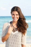 Dark-haired woman in a V-neck mesh sweater, laughing by the sea