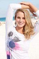 Portrait of beautiful blonde woman wearing white top standing on beach, smiling