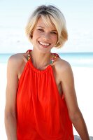 Portrait of pretty blonde woman wearing an orange top standing on beach, smiling