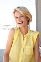 Portrait of happy blonde woman with short hair wearing yellow sleeveless top, smiling