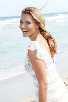 blonde Frau im weißen Kleid am Strand, lacht in die Kamera