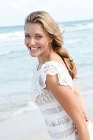 Portrait of happy blonde woman wearing white dress standing on beach, smiling
