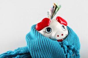 Close-up of piggy bank wrapped with blue scarf against white background