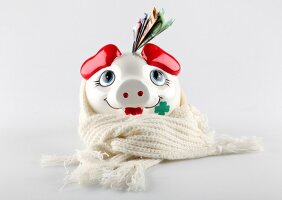 Close-up of piggy bank wrapped with beige scarf against white background