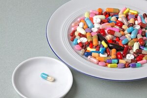 Close-up of tablets on plate and one tablet in bowl against white background