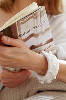 Close-up of woman wearing knitted bracelet with beads and holding a book