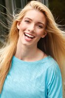 Portrait of happy blonde woman with long hair wearing light blue top, laughing