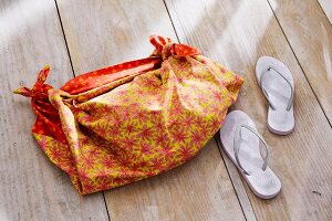 Cloth bag with flower motif and slippers by side on wooden floor