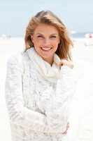 blonde Frau in weißem Rolli lächelt in Kamera, am Strand